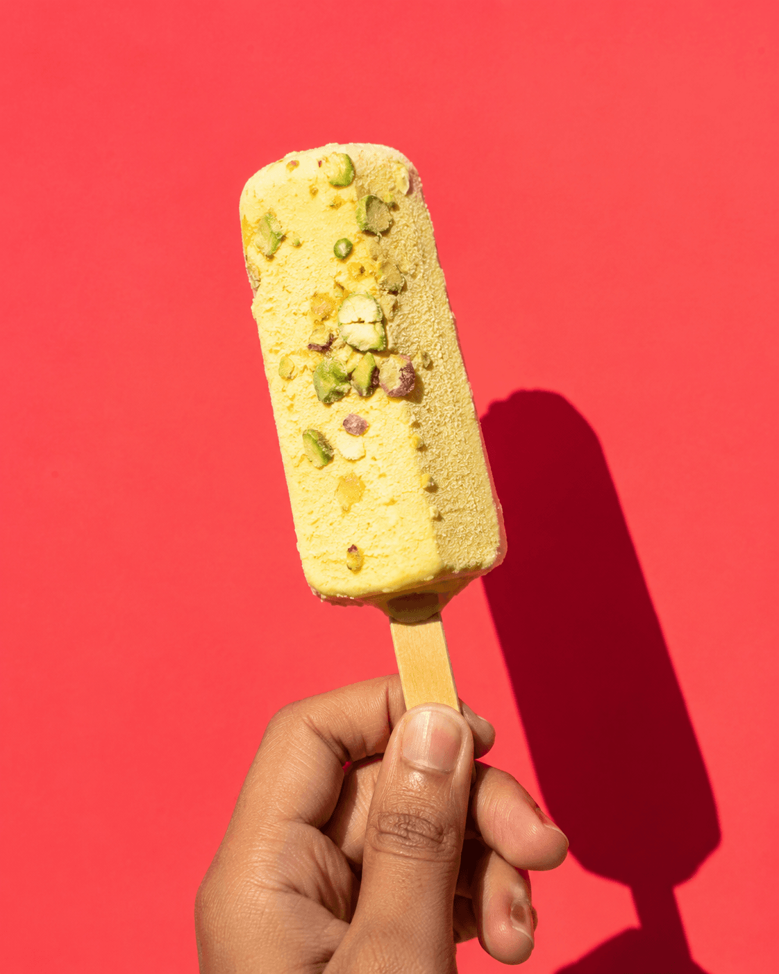 Handheld pistachio dessert bar on a coral background